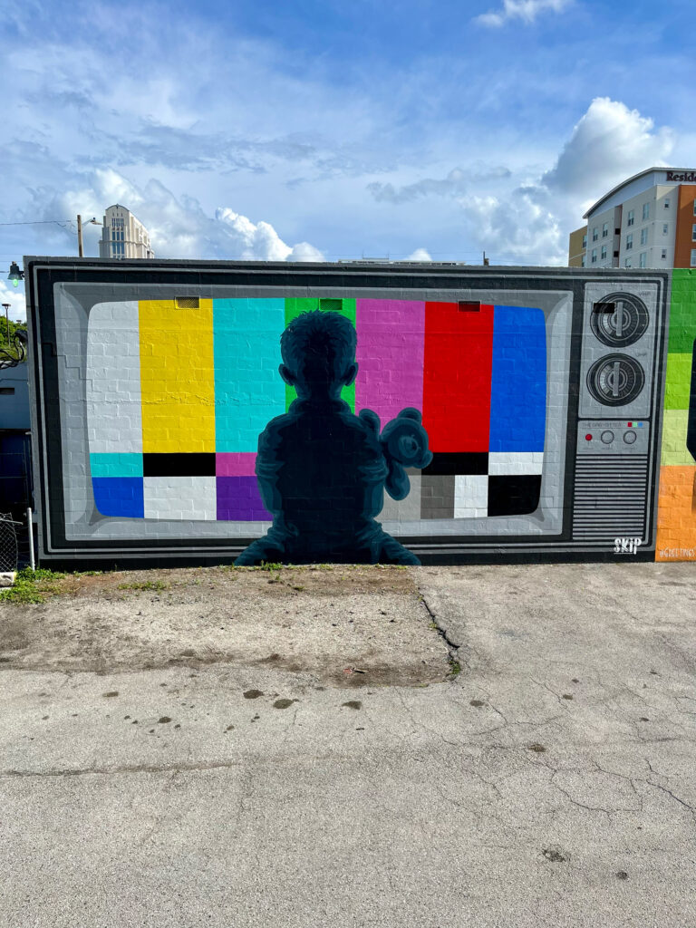 "Babysitter" mural by A Pivotal Character Artworks & Design in Orlando, Florida, which features the silhouette of a young boy in front of a television screen displaying the SMPTE color bars indicating a poor broadcasting signal.